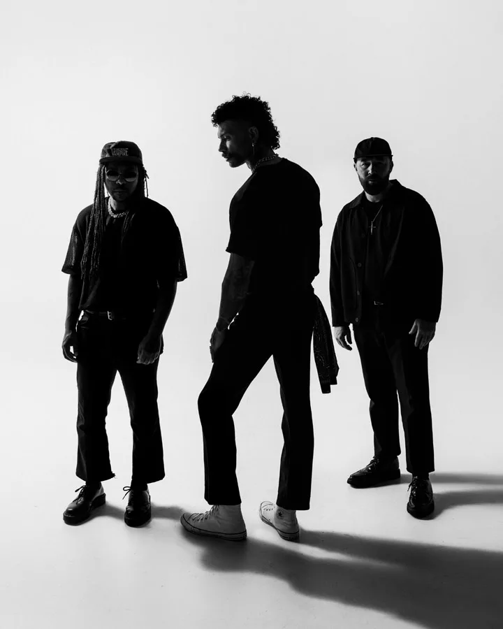 Three men standing together in front of a plain white background, all facing the camera.