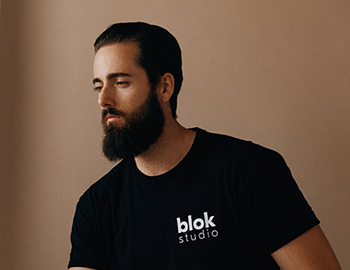 A bearded man wearing a black t-shirt is looking directly at the camera.