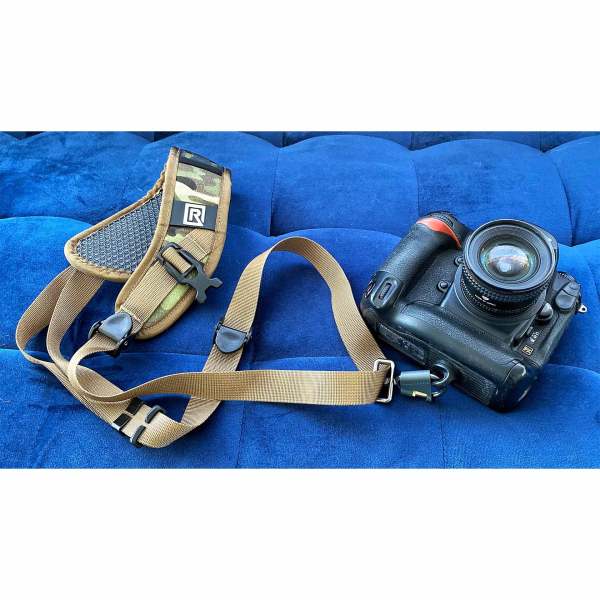 291008-SPORT-X-4 - BLACKRAPID Canada Camera strap and camera resting on a blue couch, showcasing the Sport X camera sling in a stylish setting.