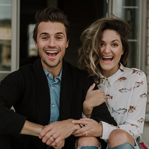 A man and woman sit on a porch, laughing together, enjoying each other's company in a warm, relaxed atmosphere.
