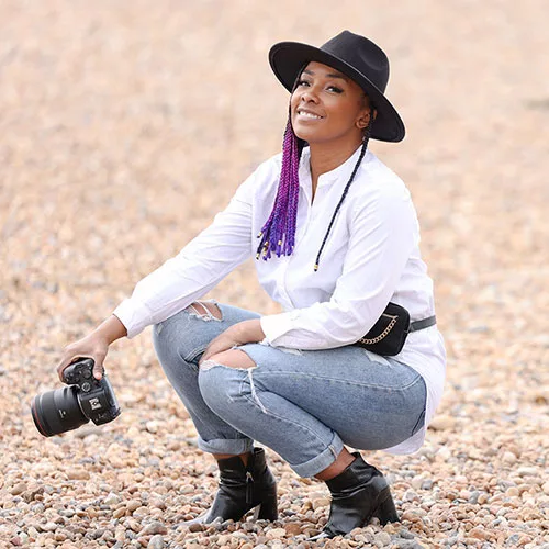 A woman with purple hair and a hat sits on the beach, enjoying the sun and the ocean view.