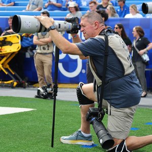 A man kneeling on a grassy field, appearing focused and engaged in an activity or observation.