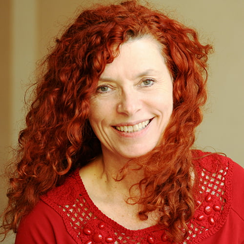 A woman with red curly hair smiles warmly at the camera.