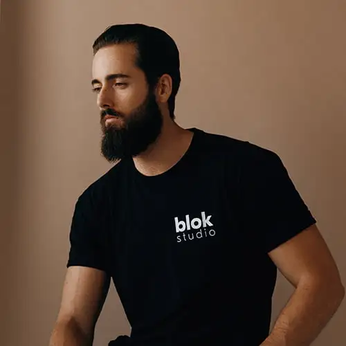 A bearded man wearing a black t-shirt is looking directly at the camera.