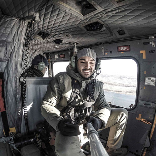 A man seated in a helicopter cockpit, focused on the controls and instruments in front of him.